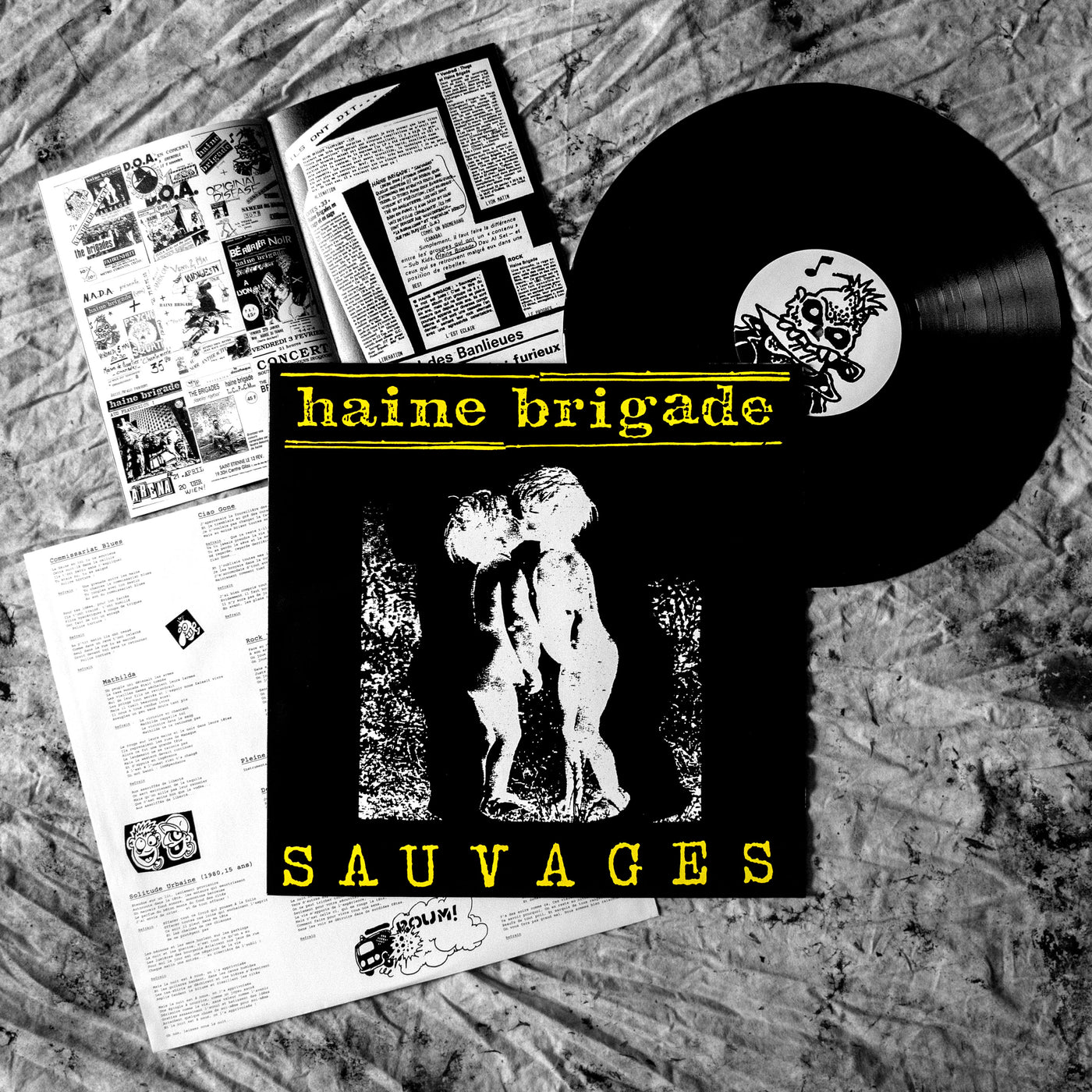pochette de l'album "Sauvages" de HAINE BRIGADE (deux enfants s'embrassent), le disque vinyle avec sur le rond central un dessin d'un squelette punk avec un couteau dans les dents, pochette intérieure avec paroles et illustrations, et livret A5 avec textes, flyers, photos et dessins.